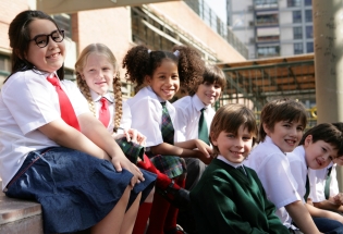 A group of smiling students in uniform sitting on some steps.  iStock image for illustrative purposes only.