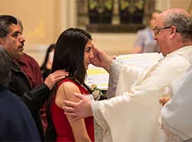 Norbertine Father Andrew Cribben, pastor of St. Willebrord Church in Green Bay, Wis., places sacred chrism oil on the forehead of Nahidaly Fiscal during the a 2014 Easter Vigil. CNS photo/Sam Lucero, The Compass