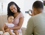 A mother and daughter pose for a photograph, which is taken by the father. 