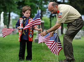 A young Boy Scout and Scoutmaster place U.S. flags at graves of military  CNS photo/Mike Crupi, Catholic Courier