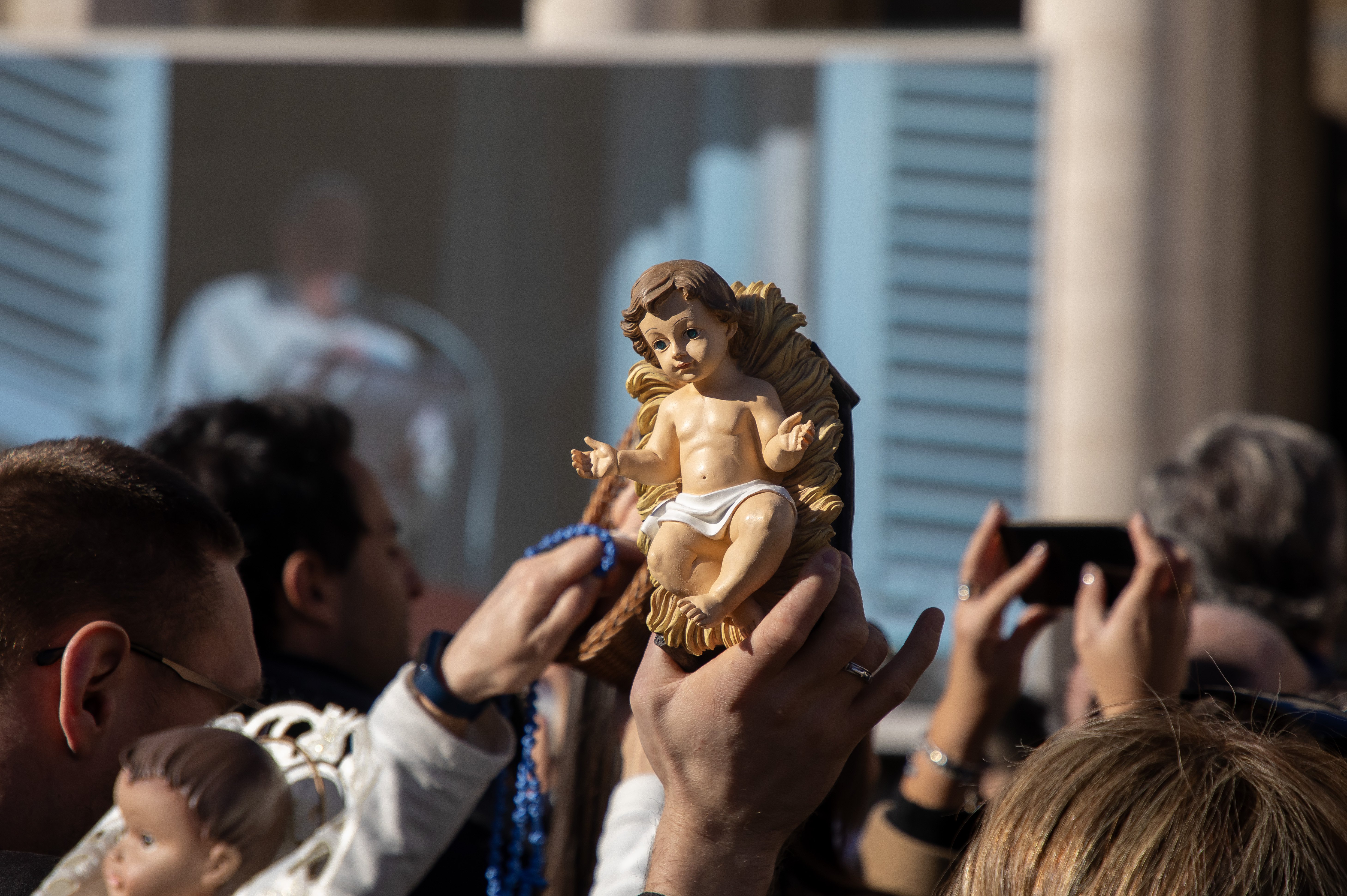 People hold up Nativity scene figurines of the baby Jesus for Pope Francis to bless.