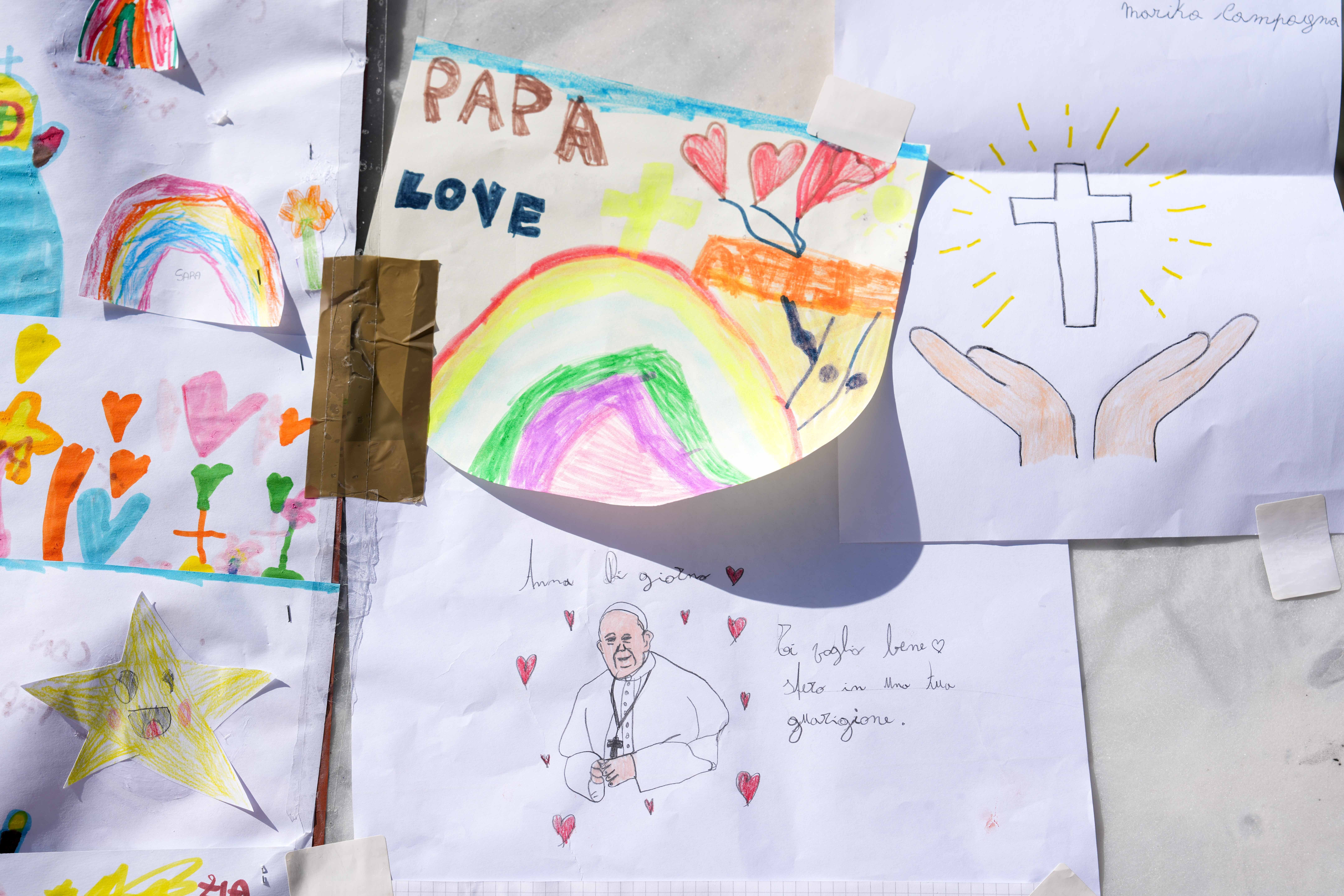 Drawings for Pope Francis are placed at the base of a statue of St. John Paul II outside Rome’s Gemelli hospital.