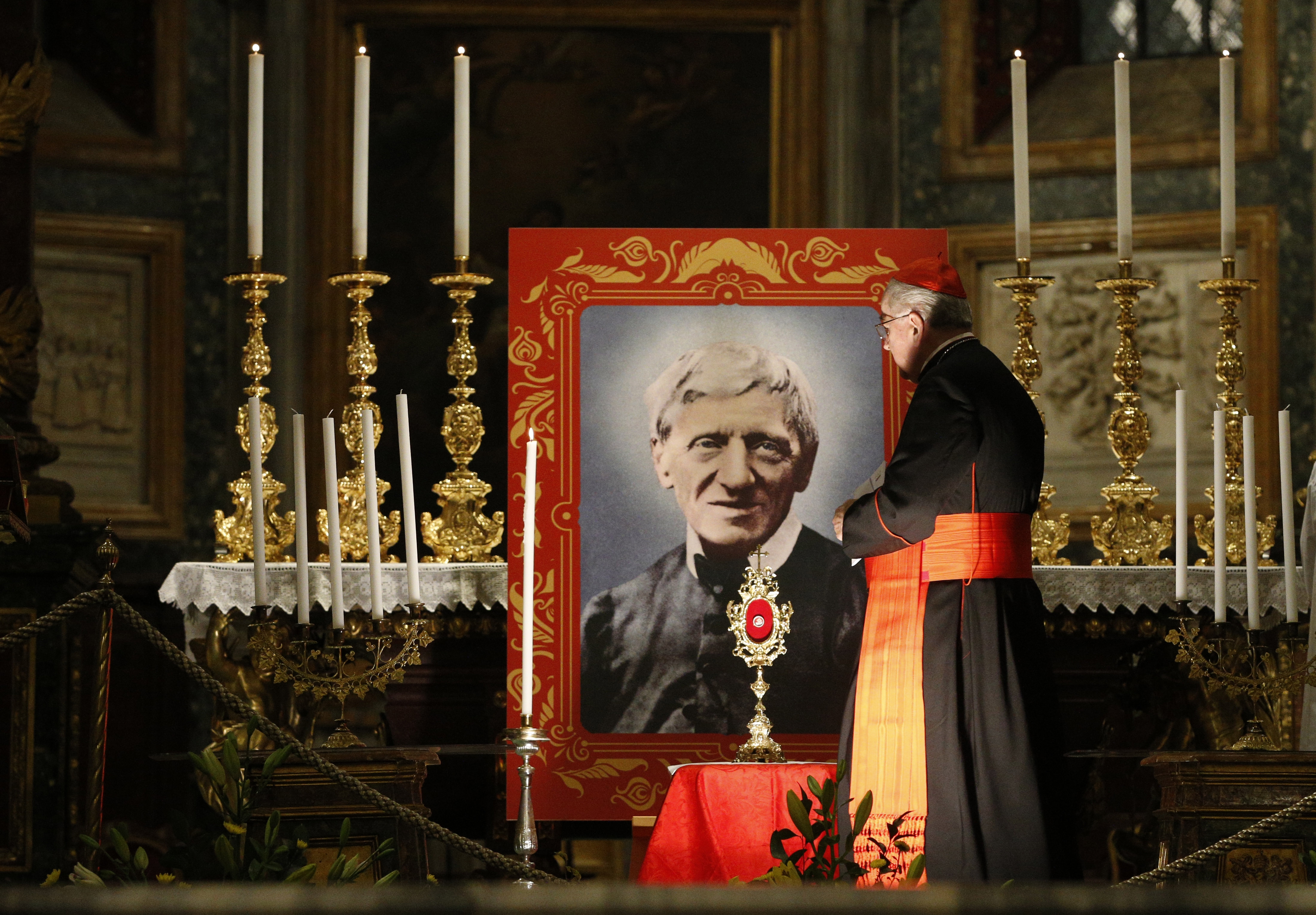 A cardinal walks by a portrait of St. John Henry Newman