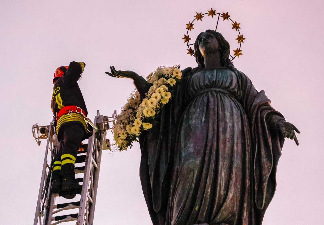 Firefighter places wreath on a statue of Mary.