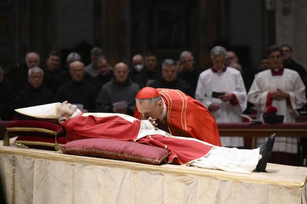 Cardinal Gambetti kisses the hands of the late Pope Benedict XVI.