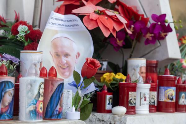 Votive candles and flowers are seen at the base of a statue of St. John Paul II outside Rome's Gemelli hospital Feb. 23, 2025, where Pope Francis is being treated for double pneumonia.