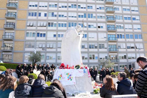 Young people and members of the House of Mary, groups associated with the Pontifical Academy of the Immaculate Conception, and others pray around a statue of St. John Paul II outside Rome’s Gemelli hospital.