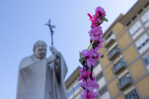 A stem of bright silk flowers can be seen at the base of a statue of St. John Paul II outside of Rome's Gemelli hospital.