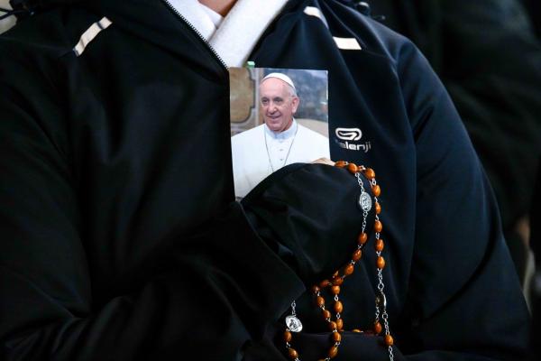 A person holds a rosary and a photo of Pope Francis as people gather in St. Peter’s Square at the Vatican to recite the rosary for Pope Francis.