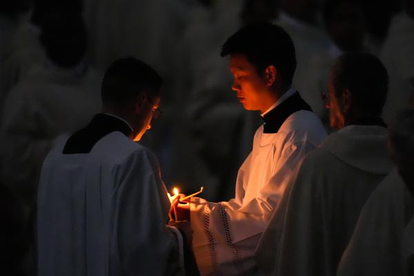 Concelebrant priests light candles from the paschal flame at the start of Easter Vigil Mass in St. Peter’s Basilica.