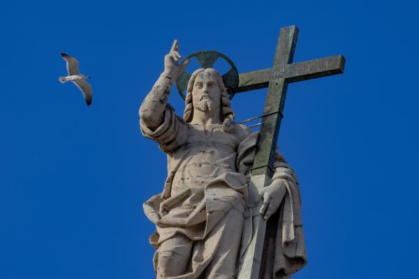 A bird flies over the statue of the Risen Christ on top of the facade of St. Peter's Basilica.