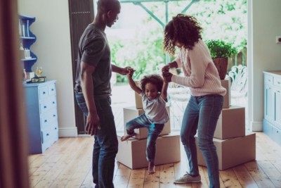 : A family—mother, father, and little girl—plays together whlie unpacking boxes in their home