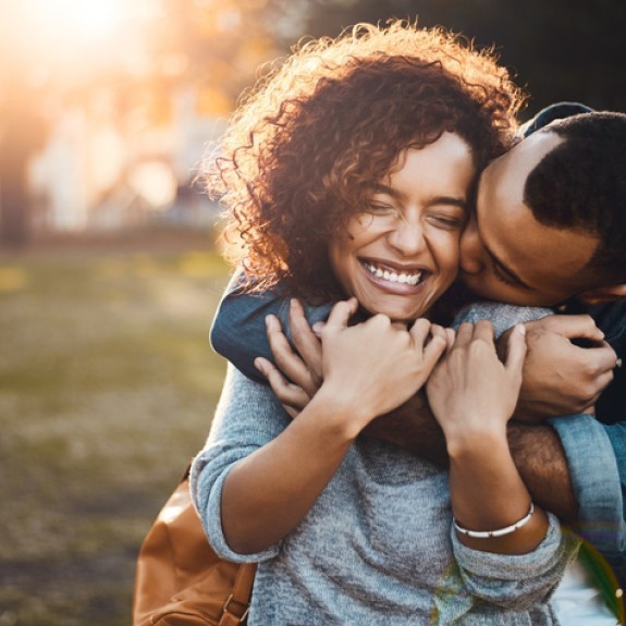 Husband hugging and kissing his wife from behind with arms wrapped around her