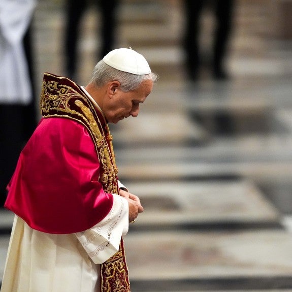 Pope Leo stands with head bowed, wearing liturgical vestments including red mozzetta