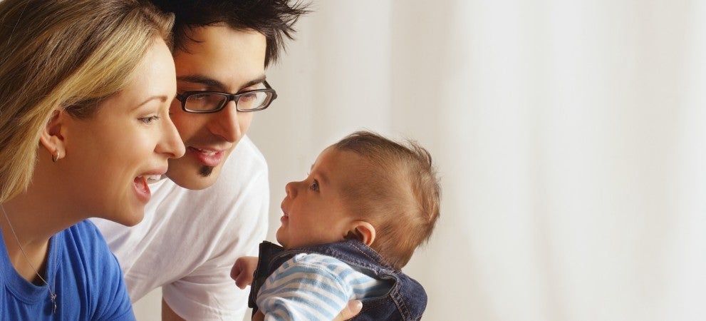 Cool young parents looking at baby (father has glasses, wife is blond, baby wearing jumper)