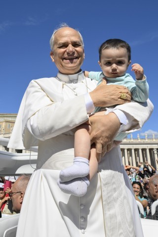 Pope Leo poses for a photo with a baby after Mass