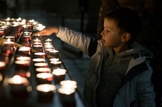 Small boy lights candle in prayer