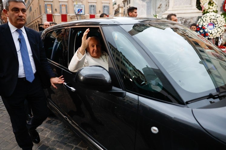 Pope Francis greets people from a car.