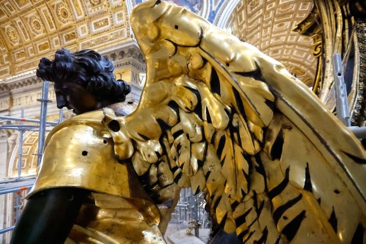 A statue of an angel with gilded wings and armor is seen surrounded by scaffolding.